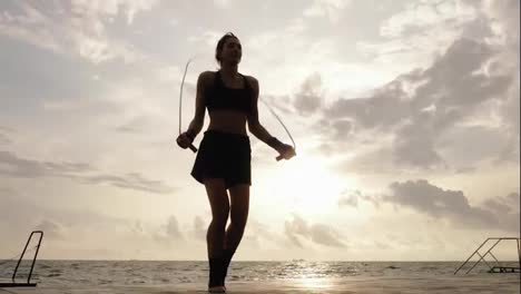 View-form-the-bottom:-Young-woman-working-out-on-the-jump-rope-against-the-sun-by-the-beach-in-slowmotion.-Lens-flare.-Girl-jumping-on-a-skipping-rope-by-the-sea.-Shot-in-4k