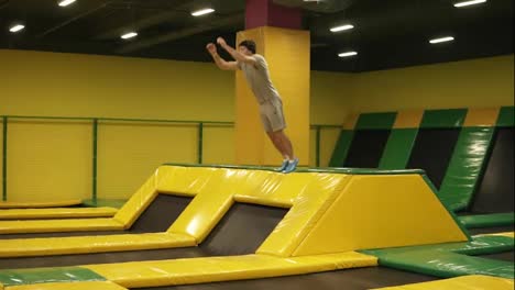 Yellow-covered-trampoline-for-young-sportive-people.-Athletic-male-performs-front-somersaults-hopping-off-the-platform.-Youth,-sport,-gymnastics.