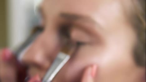 The-make-up-artist-puts-light-shiny-eyeshadow-on-a-model's-eyelids-using-two-professional-brushes.-Close-up.-Make-up-process