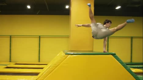 Male-gymnast-trains-on-professional-trampoline,-springs-over-the-barrier-with-the-body-twist-and-following-back-somersault.