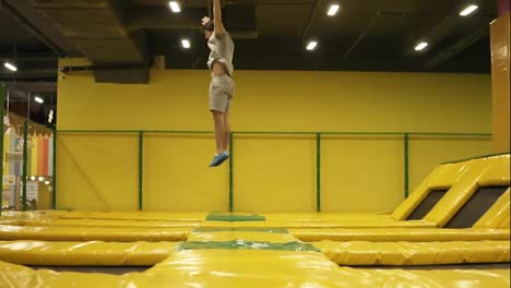 Young-male-athlete-in-beige-t-shirt-and-shorts-hopping-on-trampoline-with-somersault-and-body-twist-picking.