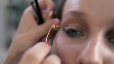 Eyes-make-up-process.-Artist-corrects-eye-line-using-a-professional-brush-with-golden-edge.-Close-up-of-a-model's-face