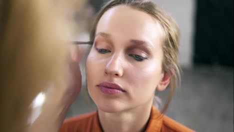 Overview-of-a-make-up-process.-Professional-make-up-artist-gently-putting-nude-eyeshadows-on-and-eyelid.-Attractive-young-blonde