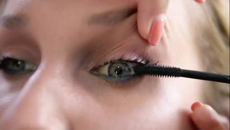 The-make-up-artist-lifts-the-eyelid-of-the-model-and-stains-eyelashes-with-mascara-stick.-Black-colour.-Close-up-view