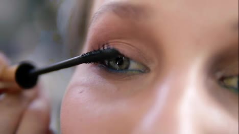 Extremely-close-of-a-young-woman's-eye.-Make-up-artist-carefully-applying-a-black-mascara.-Caucasian-model-with-green-eyes