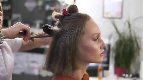 Side-view-footage-of-a-beautiful-young-woman-with-a-casual-make-up-in-beauty-salon.-Professional-hairdresser-styling-her-hair