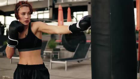 Attractive-athletic-female-boxer-in-gloves-punching-a-boxing-bag.-Workout-outside.-Female-boxer-training-in-boxing-gloves.-Shot-in-4k