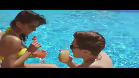 Young-adult-couple-flirting-and-talking-in-the-swimming-pool-and-drinking-cocktails.-Summertime-pool-party.-Shot-in-4k