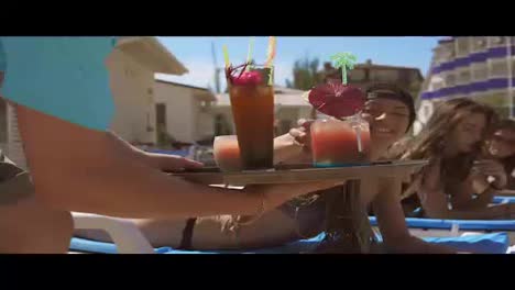 An-unrecognizable-male-waiter-bringing-cocktails-for-beautiful-young-girls-relaxing-by-the-pool.-Summertime-pool-party.-Shot-in-4k.
