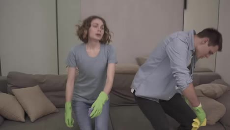 Exhausted-young-caucasian-couple-falling-down-on-a-couch-after-cleaning,-feeling-tired-after-cleaning,-swiping-sweat-from-foreheads.-Exhaling.-Wearing-green-rubber-gloves.-Slow-motion