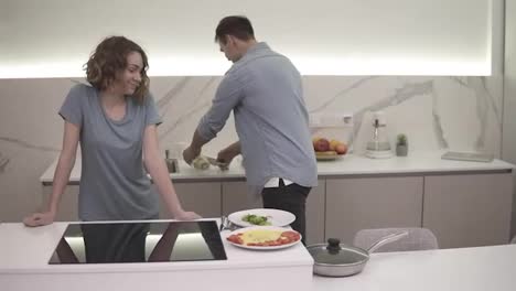 Cheerful-couple-on-bright,-white-kitchen.-They-prepared-omelette-on-pan,-together-serving-dish,-adding-chopped-celery-on-it.-Excited-and-hungry.-Slow-motion