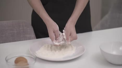 Unrecognizable-woman-takes-a-handful-of-flour-from-a-plate-lets-it-fall,-fray-through-.Closeup-of-hands,slow-motion