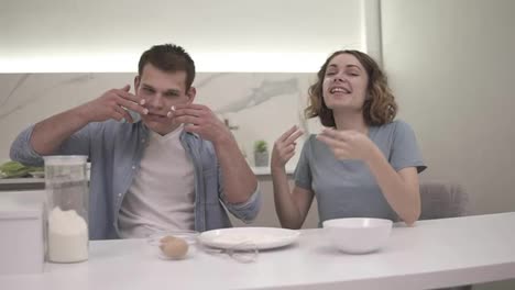 Cute-positive-couple-smudges-flour-on-their-faces-in-the-kitchen.-Happy-young-couple-fooling-around-while-cooking-food.-Slow-motion