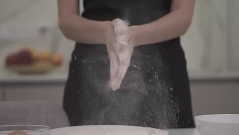 Professional-female-cook-claps-her-hands-and-powder-flies.-Concept:-the-production-of-sweets-bread-dough.-Ingredients-and-preparation-stages.-Slowmotion