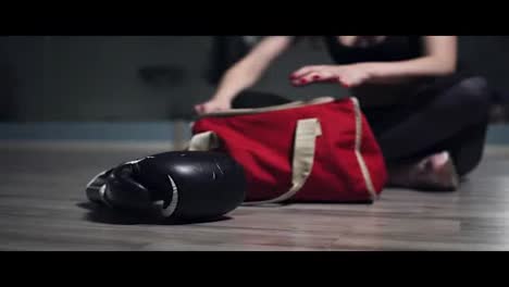 Unrecognizable-woman-sitting-on-the-floor-and-taking-from-her-bag-gloves-for-boxing,-preparing-for-training.-Shot-in-4k