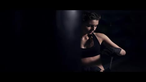 Woman-wrapping-hands-with-black-boxing-wraps-in-dark-room-and-taking-on-boxing-gloves.-Close-up-shot-in-4k