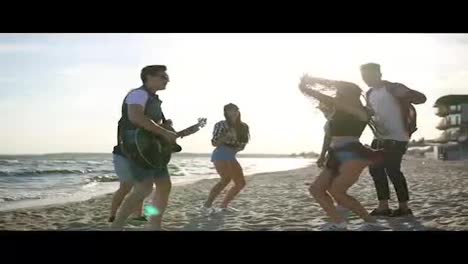 Summer-party-on-the-beach.-Young-friends-drinking-cocktails,-dancing-in-the-cirkle,-playing-guitar,-singing-songs-and-clapping-on-a-beach-at-the-water's-edge-during-the-sunset.-Slowmotion-shot