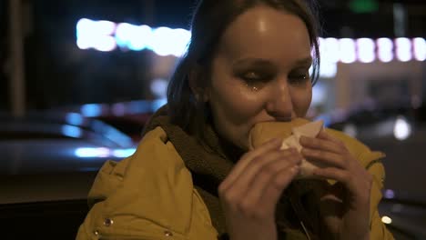 Happy-smiling-girl-with-a-sparkles-on-her-face-taking-hamburger-on-a-night-street.-Handheld-footage