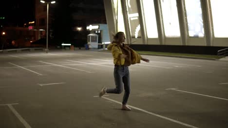 Slim,-delicate-girl-in-grey-pants-and-yellow-coat-is-dancing-and-has-fun-on-the-parking-outside
