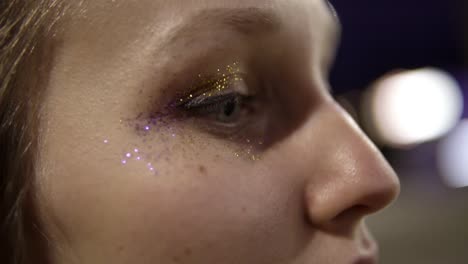 Close-up-footage-of-a-beautiful-girl-with-purple-and-gold-sparkles-on-her-eyes.-Closes-eyes,-blink.-Outside