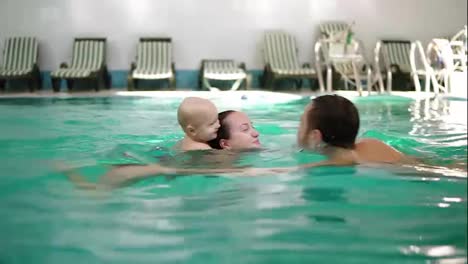Young-family-swimming-in-the-pool-together-with-his-cute-little-child.-The-boy-is-swimming-on-the-back-of-his-mother.-Happy-family-having-fun-in-the-pool