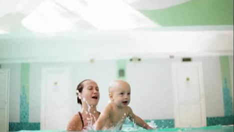Young-mother-is-lifting-her-son-from-the-water-holding-his-feet-while-teaching-him-how-to-swim-in-the-swimming-pool.-Happy-little-boy-and-his-mother-are-laughing-and-having-fun