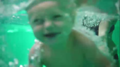 Cute-blonde-toddler-is-diving-under-the-water-while-his-mother-is-holding-him.-His-mother-is-teaching-him-how-to-swim.-An-underwater-shot