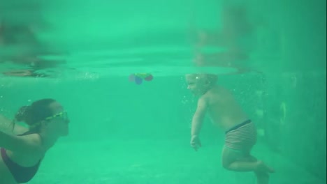An-underwater-shot-of-cute-blonde-toddler-swimming-under-the-water-together-with-his-mother-in-the-swimming-pool.-Then-his-mother-is-lifting-him-from-the-water.-His-mother-is-teaching-him-how-to-swim
