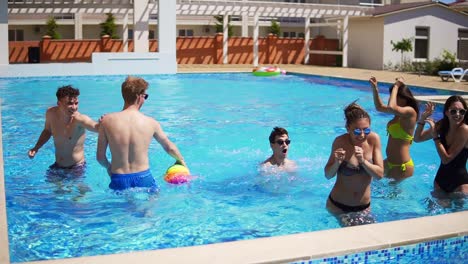 Group-of-young-friends-playing-volleyball-in-the-swimming-pool.-Summertime-pool-party.-Slow-Motion-shot