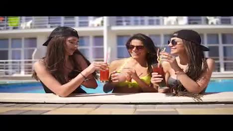Beautiful-young-girls-in-sunglasses-drinking-cocktails-relaxing-by-the-pool.-Summertime-pool-party.-Slowmotion-shot