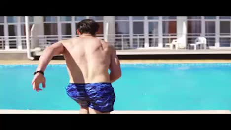 Back-view-of-young-athletic-man-in-swim-shorts-running-and-jumping-to-the-swimming-pool.-Slowmotion-shot.