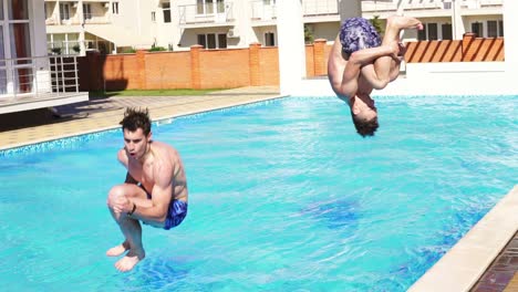 Two-young-athletic-men-in-swim-shorts-running-and-jumping-to-the-swimming-pool-turning-around.-Slow-Motion-shot