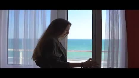 Woman-with-long-hair-opening-balcony-doors-and-looking-out-at-the-sea.-Enjoying-the-sea-view-outside.-Slowmotion-shot