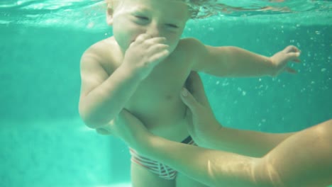 Adorable-toddler-is-swimming-under-the-water-in-the-swimming-pool-together-with-his-mother.-and-underwater-shot.-Slow-Motion