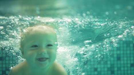 Happy-smiling-toddler-is-jumping-and-diving-under-the-water-in-the-swimming-pool.-and-underwater-shot.-Slow-Motion