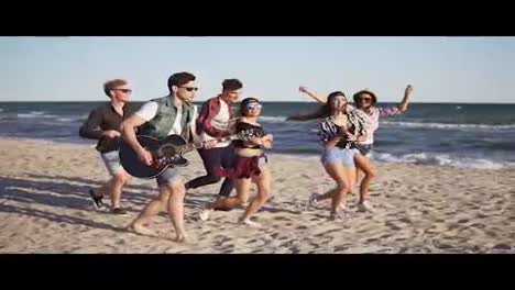 Group-of-young-hipster-friends-walking-and-dancing-together-playing-guitar-and-singing-songs-on-a-beach-at-the-water's-edge.-Slowmotion-shot