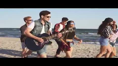 Gruppe-Junger-Hipster-Freunde,-Die-Gemeinsam-An-Einem-Strand-Am-Wasser-Spazieren-Gehen-Und-Tanzen,-Gitarre-Spielen-Und-Lieder-Singen.-Zeitlupenaufnahme