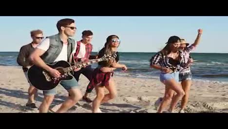 Hipster-friends-walking-and-dancing-together-playing-guitar-and-singing-songs-on-a-beach-at-the-water's-edge.-Slowmotion-shot