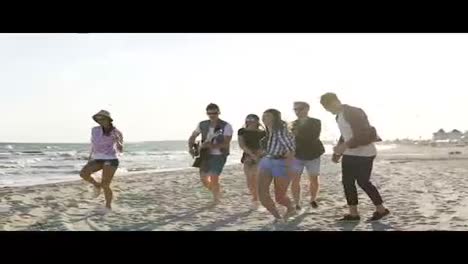 Young-boys-and-girls-clapping,-dancing-together-playing-guitar-and-singing-songs-on-a-beach-at-the-water's-edge.-Slowmotion-shot
