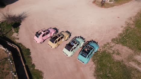 Aerial-rotation-view-of-some-colored-vintage-cars-on-a-dirt-road-in-a-queue-used-as-tourist-attraction,-Citroën-CV2