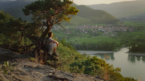 male-looking-at-the-golden-hour-sunset-under-a-tree,-mountain-landscape-background,-river-danube-valley,-overview,-looking-out,-peaceful-digital-detox,-outdoor-nature,-overstimulation-detox,-travel