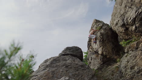 Kletterer-Springt-Vom-Grat-Zum-Rand,-Bergsteigen,-Freeclimbing-Mann,-Bouldern-In-Felsiger-Umgebung,-Abenteuerlich,-Spektakulär,-Solo,-Action-Aufnahme,-Statische-Filmische-Weite-In-Sonniger-Landschaft