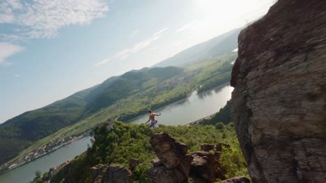 guy-on-top-of-mountain-ridge,-fast-drone-FPV,-aerial-shot-with-speed,-king-of-the-world-pose,-mountainclimber,-person-on-top-of-hill,-danube-river-valley-landscape-overview,-flying-around,-flying-fast