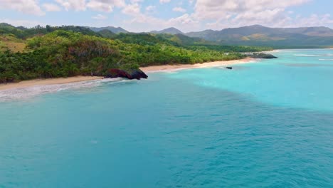 Langsame-Luftaufnahme-Entlang-Des-Karibischen-Meeres-Und-Der-Sandigen-Playa-Breman-Mit-überwucherter-Hügellandschaft-Im-Hintergrund---Tropische-Insel-Der-Dominikanischen-Republik