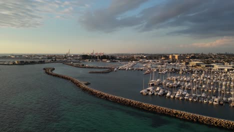 Aerial-approaching-shot-of-Fishing-Boat-Harbour-in-Fremantle-City-during-golden-hour---Western-Australia-and-industrial-port-in-background