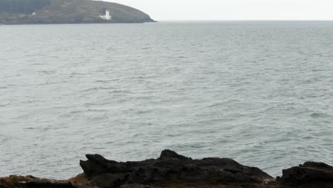 Looking-out-to-sea-with-St-Anthony-Head,-Lighthouse-in-background-from-Pendennis-head-with-Jagged-rocks-in-foreground