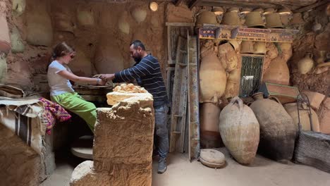 Tunisian-potter-teaches-tourist-little-girl-with-red-hair-to-work-clay-with-pottery-wheel