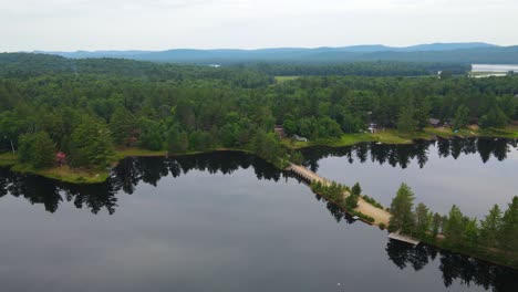 drone-shot-of-pine-trees-reflecting-across-the-still-waters-of-a-lake-in-the-mountains-of-upstate-New-York