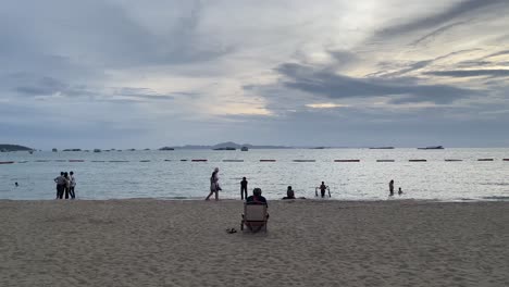 Scene-of-a-man-sitting-on-the-beach-chair-enjoying-the-sea-view-and-people-strolling-by-the-beach-in-Pattaya,-Thailand