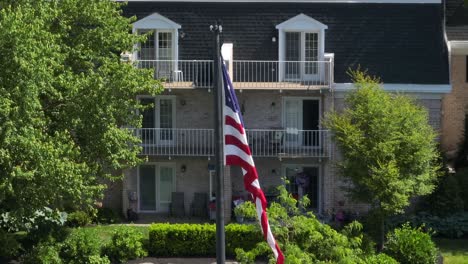 Panoramic-view-of-an-American-flag-gently-blowing-in-the-breeze-in-a-courtyard-in-front-of-an-apartment-complex-on-a-clear-summer-day